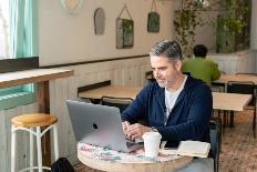 Man sitting in a coffee shop and researching the role of peer support in combating veteran depression on his laptop.